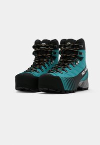 Par de botas de caminhada em teal e preto com atacadores pretos e laranja, apoio alto para o tornozelo e sola rugged, posicionadas lado a lado.