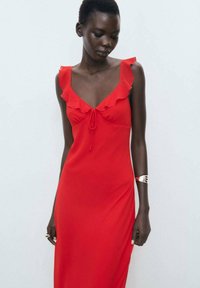Robe sans manches rouge avec des accents à volants, détail à nouer à l'avant, silhouette ajustée, texture de tissu lisse et longueur maxi.