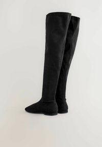 Schwarze Überknie-Stiefel aus Wildleder mit einer glatten Textur, spitzer Zehenpartie, flacher Sohle und schlichtem, nahtlosem Design.