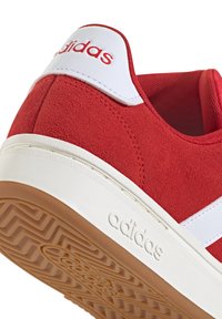 Rote Wildleder-Sneaker mit weißen Akzenten, ausgestattet mit einer strukturierten, sandfarbenen Gummisohle und einem eingeprägten Logo an der Seite. Glatter, weiß gepolsterter Absatz.
