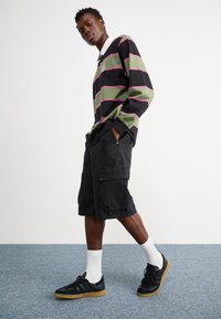 Koszula z długim rękawem w paski w kolorze zielonym, czarnym i różowym; czarne szorty cargo z bocznymi kieszeniami; czarne trampki; białe skarpetki. Prosty wzór.