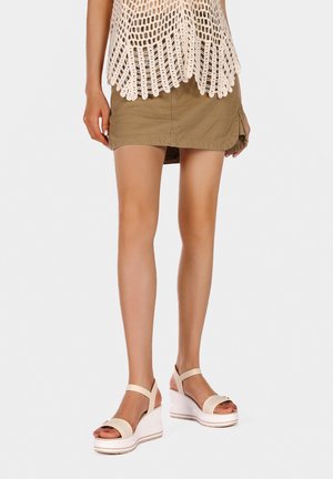 Sandali wedge bianchi con cinturino beige, design open toe e piattaforma testurizzata. Indossati con una gonna khaki e un top all'uncinetto.