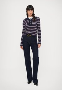 Μπλούζα με μακριά μανίκια σε ναυτικό και λευκό ριγέ, με γιακά και κουμπιά, σε συνδυασμό με σκούρα μπλε τζιν καμπάνα και μαύρα παπούτσια.