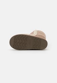 Botte en daim marron avec une semelle en caoutchouc texturée ondulée, présentant un accent tressé le long du bord supérieur. Design simple, sans quincaillerie visible.