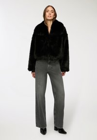 Czarna kurtka z sztucznego futra, krótka, z szerokim kołnierzem, w połączeniu z szarymi dżinsami o wysokim stanie i prostych nogawkach oraz czarnymi botkami na słupku.