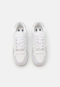 Ett par vita låga sneakers med perforerat tåparti och snörning, visade uppifrån på en vit bakgrund.