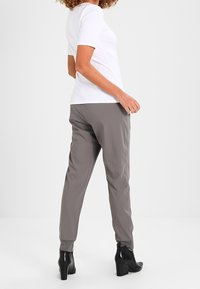 Graue, taillierte Hose aus leichtem Stoff, kombiniert mit einem weißen Oberteil mit kurzen Ärmeln und schwarzen, hochhackigen Stiefeletten, von hinten betrachtet.