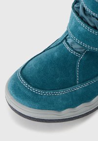 Teal semsket støvel med teksturert overflate, som har hvite sømmer, polstret krage, og grå gummisåle for grep og holdbarhet.