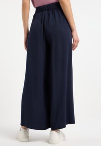 Pantaloni ampi color blu scuro realizzati in un materiale liscio, con vita elasticizzata, dal taglio comodo e senza motivi o decorazioni visibili.