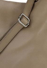 Beige leren handtas met een getextureerd oppervlak. Voorzien van een zilveren metalen gesp op de verstelbare band, die de structuur van de tas benadrukt.