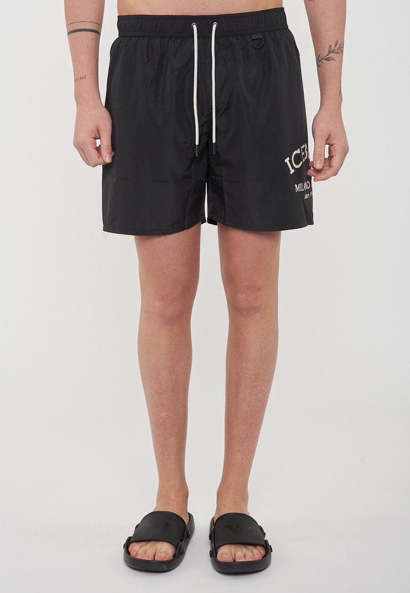 Pantaloni da bagno neri con cintura elastica e cordino; presentano un logo stampato sulla gamba sinistra e un tessuto morbido e leggero.