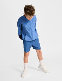 Blå atletisk jacka och shorts set i slät tyg. Jackan har dragkedjeslupp och kontrasterande svarta detaljer; shortsen är över knäna.