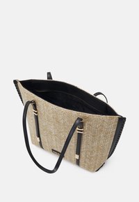 Tote bag featuring a textured beige woven exterior with black leather accents, dual black handles, and an open top revealing a black interior.
