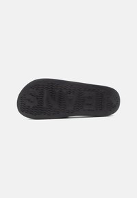 Black rubber shoe sole with zigzag traction pattern and raised logo. Smooth texture with a rounded shape, intended for comfort and durability.