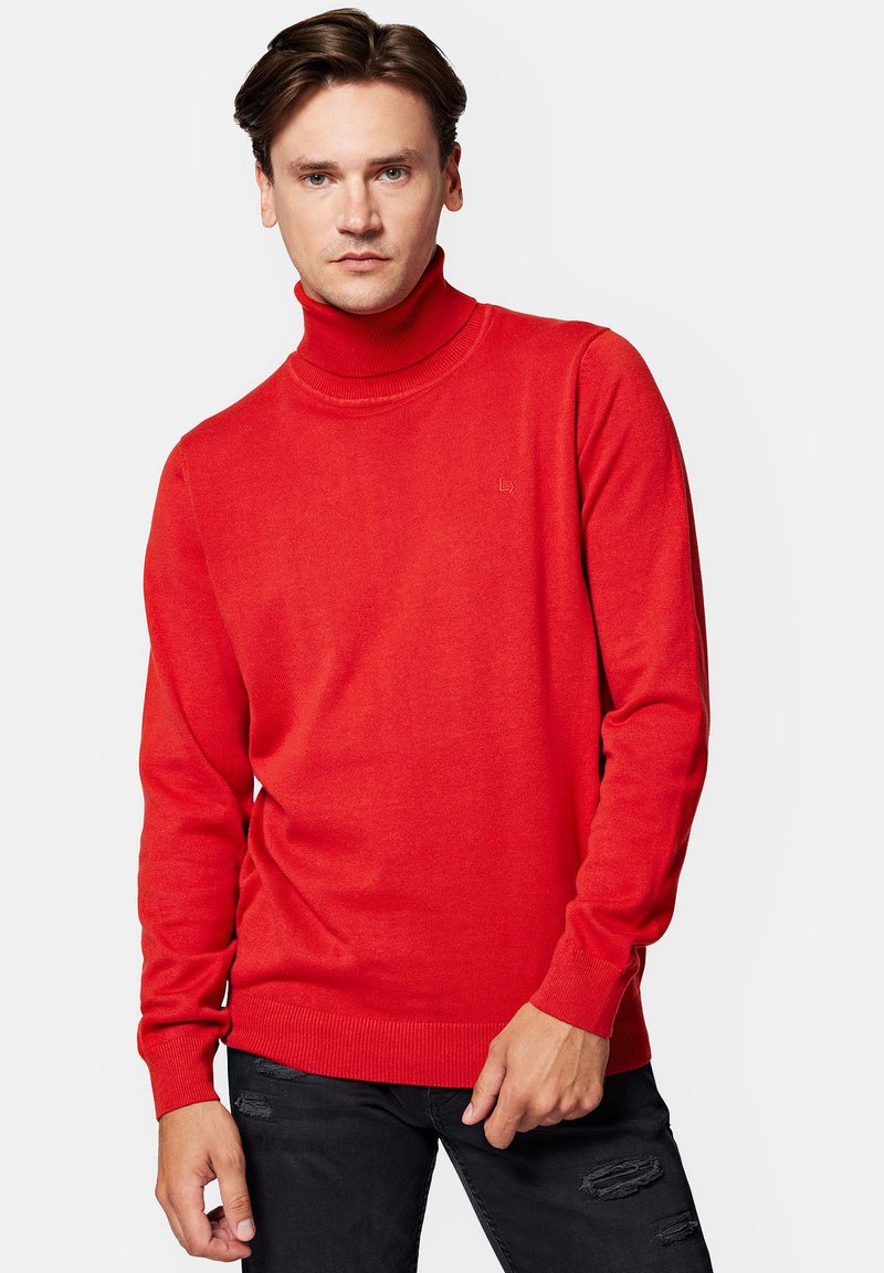 Czerwony sweter z golfem, wykonany z dzianiny. Posiada ściągacze na rękawach i dole, z małym logo na klatce piersiowej. Noszony z czarnymi, zniszczonymi dżinsami.