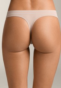 Svetlo taupe tanga z gladkim, elastičnim materialom. Ima širok, mehak pas in minimalno pokritost hrbta, ki se nizko prilega bokom.