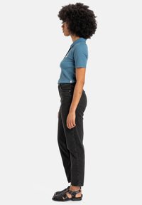 Blue polo shirt, black high-waisted jeans, and black strappy sandals. Displaying a side view, emphasizing fit and color contrast.