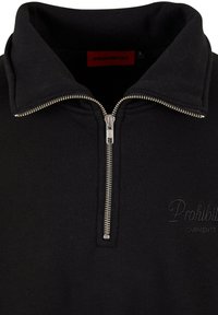 Svart hettegenser med glidelås krage, med en sølvfarget glidelås og brodert logo i en lysere nyanse. Mykt stoff med en jevn tekstur.
