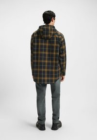 Sort og brun ternet skjorte med hætte, med lange ærmer, buet kant og knapstolper, parret med grå jeans og sorte sko.