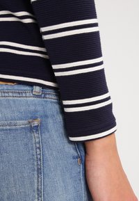 Sudadera de rayas en azul marino y blanco de manga larga con textura acanalada, combinada con jeans de mezclilla azul claro, mostrando detalles de los puños y los bolsillos.