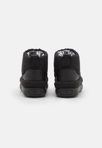 Botas negras hasta el tobillo con un material exterior suave, forma redondeada, puño elástico y suela de goma texturizada. El interior presenta un forro con marca.