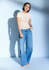 Cremefarbenes enganliches T-Shirt kombiniert mit lockeren hellblauen Jeans. Die Jeans verfügen über ein klassisches Fünf-Taschen-Design und einen geraden Schnitt.