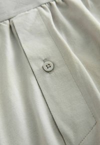 Jasnoszara tkanina o gładkiej fakturze, z guzikami i fałdami, prezentująca prosty design i czyste linie.