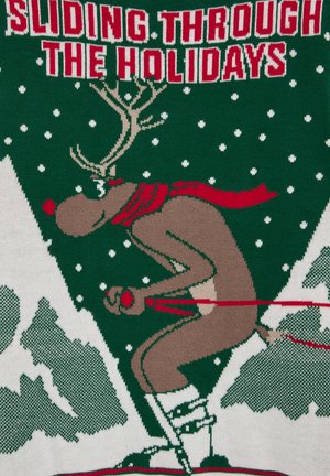 Suéter de punto con un reno esquiador en marrón con una bufanda roja, sobre un fondo verde con copos de nieve blancos y formas de montañas. El texto arriba dice "DESLIZÁNDOSE A TRAVÉS DE LAS FIESTAS."