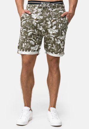 Pantaloni corti verdi con un motivo di foglie tropicali bianche, realizzati in tessuto leggero. Presentano risvolti, tasche laterali e una cintura regolabile con cordino.