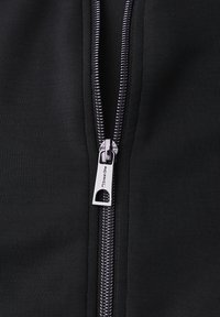 Černá bundá na zip s kovovým zipem a značkovým táhlem, která vykazuje hladkou texturu látky a čisté detaily šití.