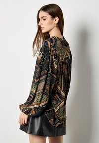 Blusa a maniche lunghe in blu scuro e verde con motivi geometrici e floreali. Presenta un design con spalle arricciate e un tessuto leggero.