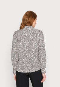 Langsleeve blouse in lichte stof, met een witte basis en zwart en gekleurde spetterprint, een ronde kraag en geplooide mouwdetails.
