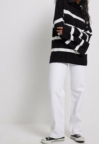 Schwarz-weißer gestreifter Pullover mit langen Ärmeln, kombiniert mit weißen geraden Jeans und schwarzen Leinenschuhen.