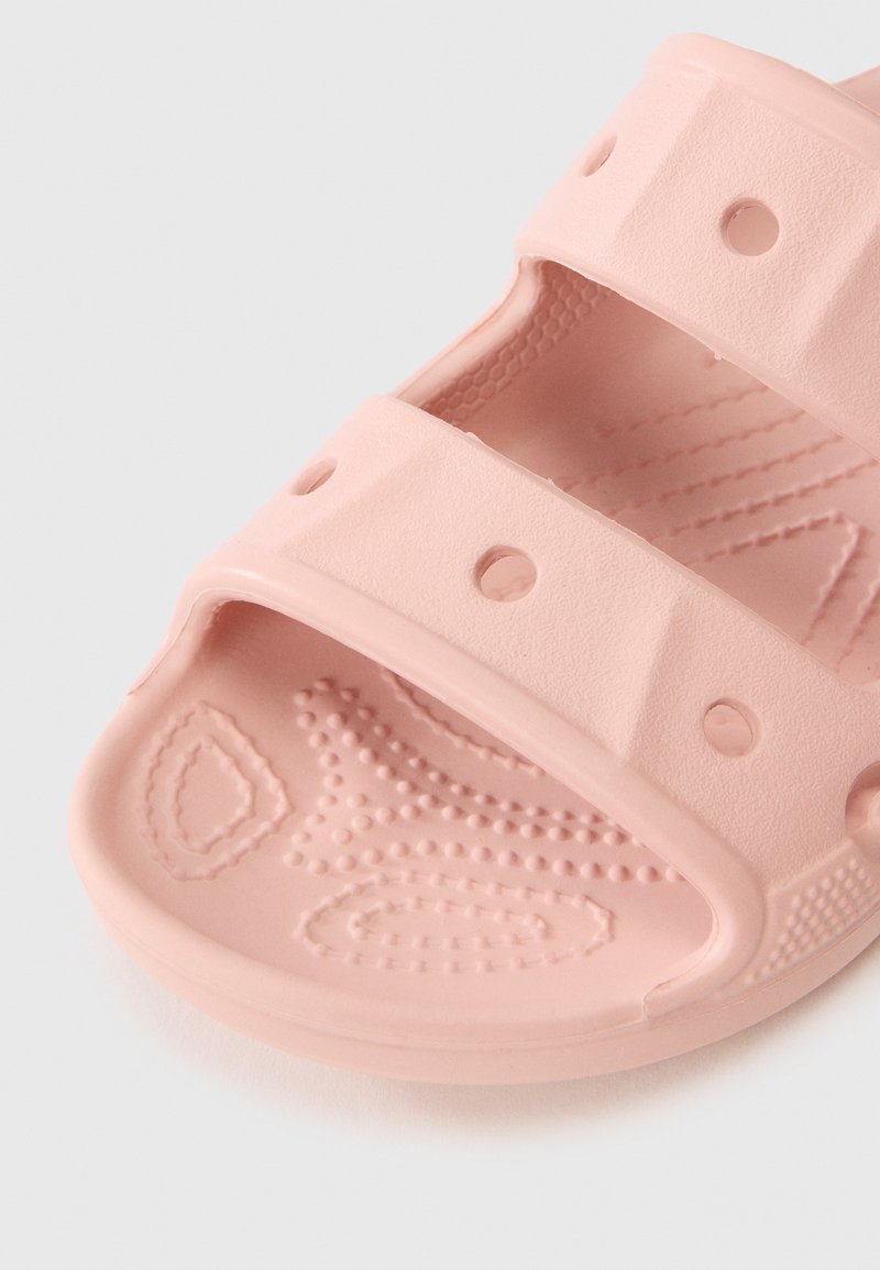 Sandale en caoutchouc rose avec deux larges sangles, découpes circulaires, semelle intérieure texturée avec motifs et finition lisse.