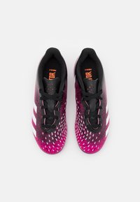 Par de botas de fútbol negras y rosas con rayas blancas, cordones negros y texto en la plantilla de color naranja, vistas desde arriba sobre un fondo blanco.