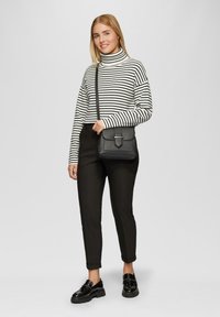 Zwart-wit gestreepte coltrui, zwarte slim-fit broek en een gestructureerde zwarte schoudertas met klep, gedragen met glanzende schoenen.