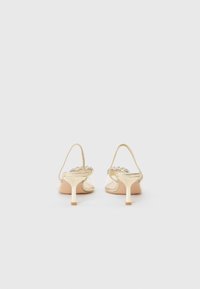 Beige heeled sandals with a transparent upper and thin strap, featuring beaded accents and a flared heel for added support.