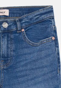 Blå denimjeans med et klassisk fem-lommers design, som har kobbernitter, syet detalj og et lærrett merke på midjen.