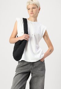 Tricou alb fără mâneci cu text imprimat, geantă de umăr neagră matlasată și blugi gri largi. Texturi line și paletă de culori neutră.