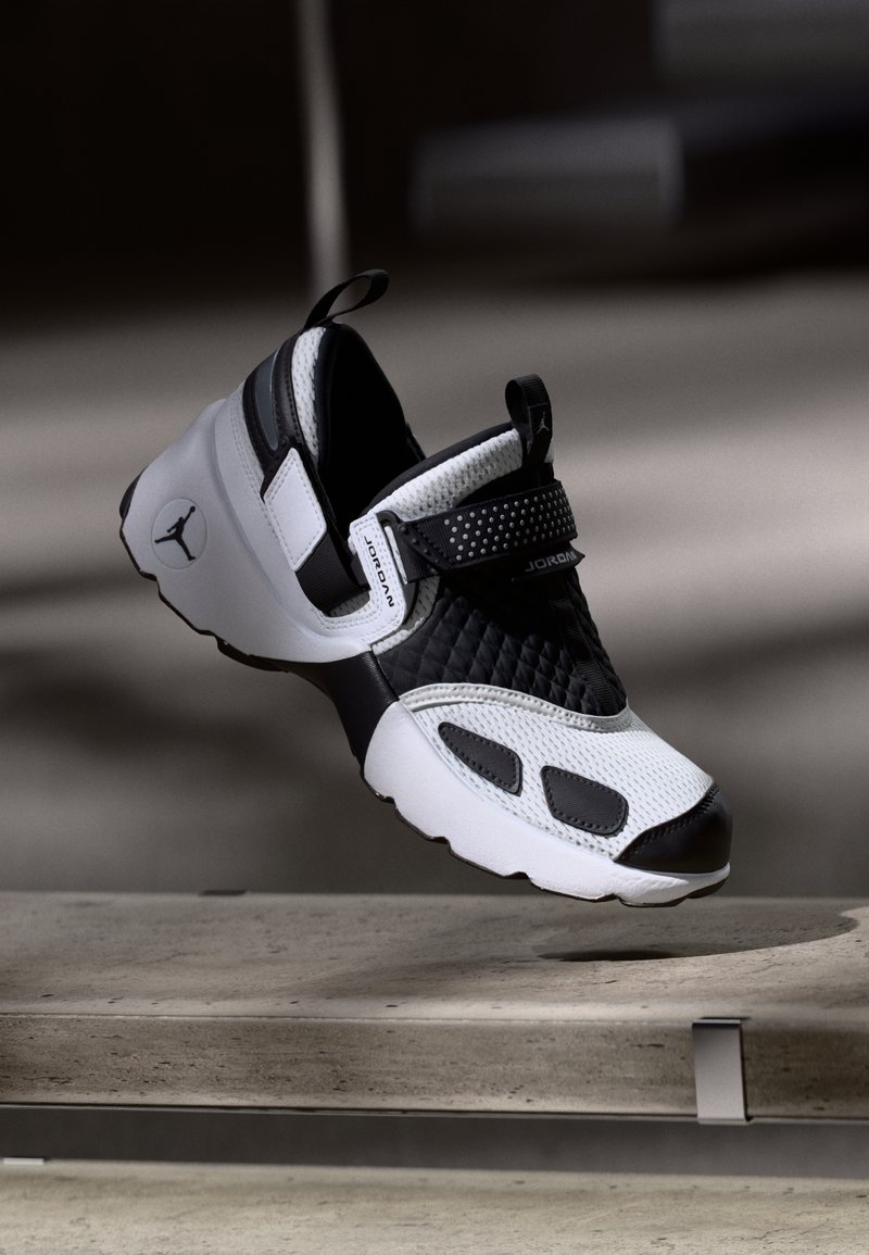 Black and white Jordan sneaker suspended above a concrete bench in soft, neutral lighting.