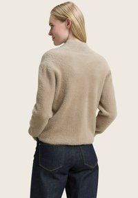 Beige, gestructureerde, langemouwtrui met een ronde hals, gecombineerd met donkerblauwe spijkerbroek. De stof ziet er zacht en comfortabel uit.