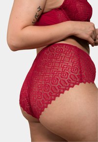 Culotte en dentelle rouge avec un motif géométrique, des bords festonnés et une texture semi-transparente, conçue pour un ajustement près du corps et le confort.