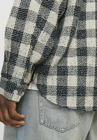 Woven checkered shirt in navy and cream, featuring a buttoned cuff, textured fabric, and a slightly oversized fit on a casual denim background.