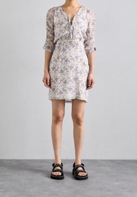 Floral dress with a V-neckline, long sleeves, and elastic waist; features lavender and green patterns. Black sandals with buckles.