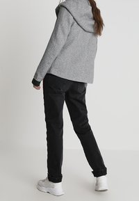 Grijze hoodie met een grote capuchon, groene accenten, gecombineerd met zwarte broek met boorden en witte sneakers, gezien vanaf de achterkant.