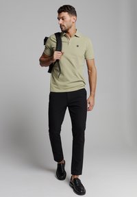 Lichtgroene polo met een kraag en een klein logo, gecombineerd met zwarte slim-fit broek en zwarte schoenen. Minimalistisch ontwerp, geen patronen.
