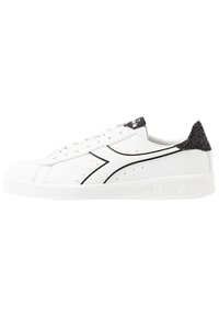 Bílá nízká teniska s černým glitrovým patkem, černým logem na boku a bílými tkaničkami.