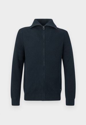 Donker marineblauw fijngebreide trui met een volledige ritssluiting, een hoge kraag en geribbelde structuur, afgebeeld tegen een lichte achtergrond.