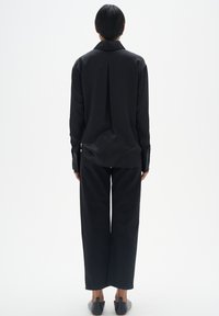 Schwarzes Langarmshirt aus glattem Stoff, mit einem Rückenfalten, kombiniert mit weiten schwarzen Hosen. Schlichtes Design, ohne Muster oder Akzente.