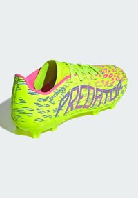 Botín de fútbol color amarillo neón con acentos rosas y diseño gráfico, superficie texturizada, cierre con cordones y suela con cinco tacos para tracción.